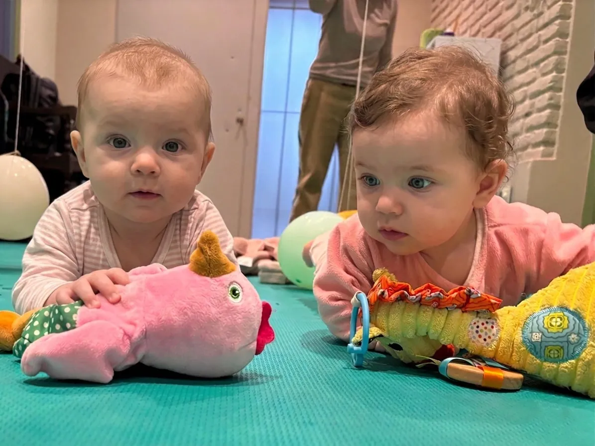 Bebes dos y tres meses acostados panza abajo jugando con peluche en alfombra de goma